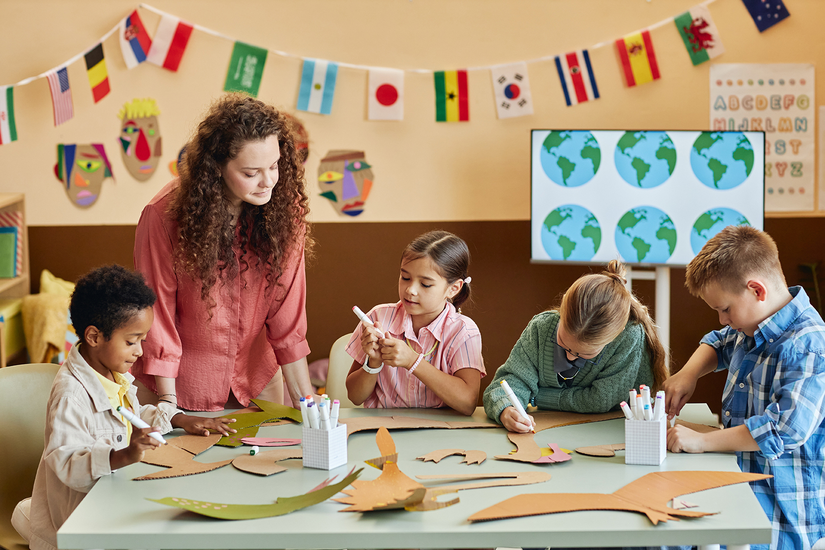 Multiethnic group of children cutting cardboard during art class making dinosaur figures and learning about Earth history